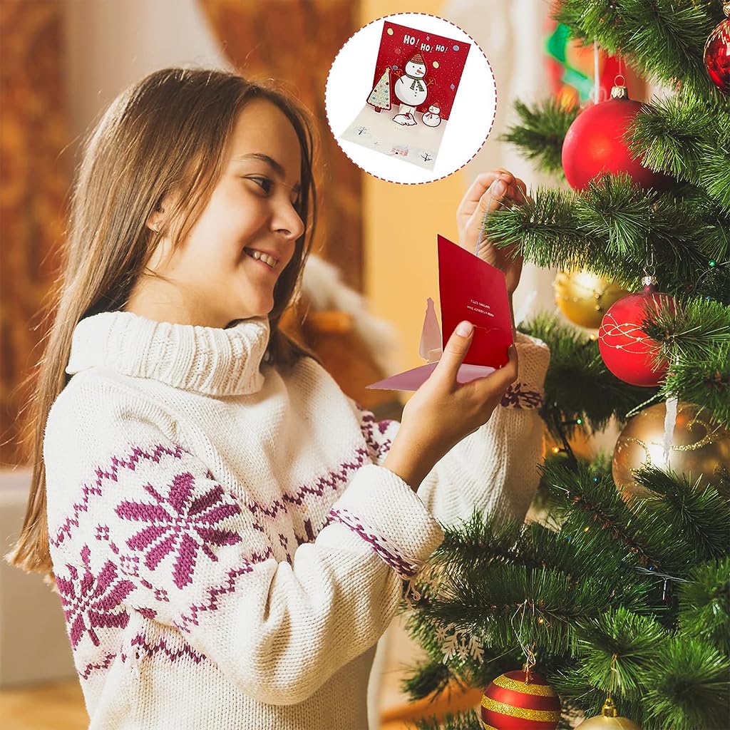 Girl holding red paper 3D Christmas cards with pop-up snowman at tree